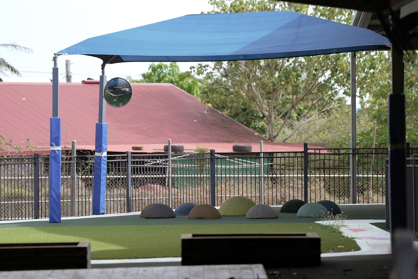 An outdoor play area at a childcare with a shade cloth and coloured mounds.