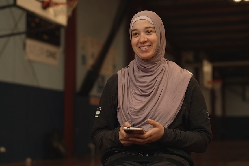 Reema El Qassem, wearing a hijab, smiles as she holds her phone.