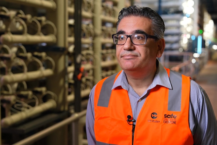 A man with glasses and a high-vis vest stands inside a desalination plant.