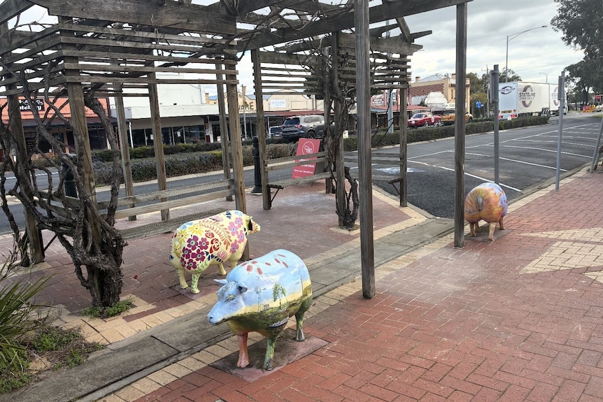 Three sheep statues with brightly painted patterns and landscapes on them stand alongside Kaniva's main street.