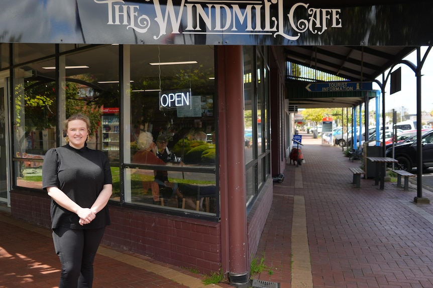 A woman stranding in front of a corner building, bearing the sign "The Windmill Cafe" on the large window.