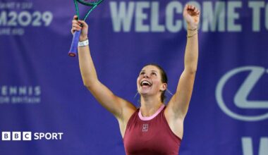 Hannah Klugman, in maroon tennis outfit, celebrates with both arms aloft as she looks upwards