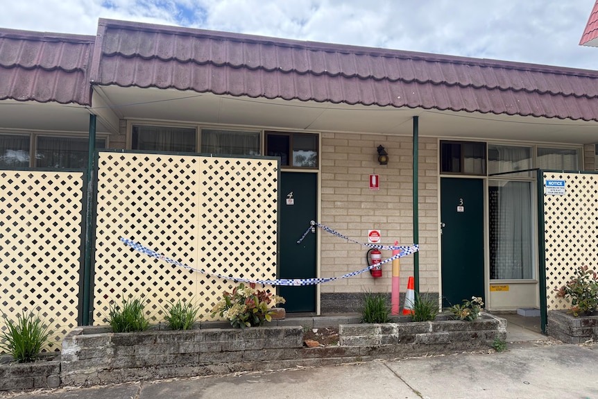 Police tape tied across a cream-coloured motel building which has a green door.