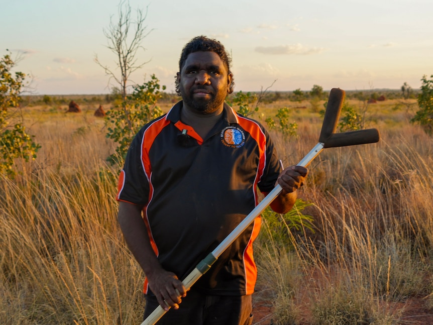 An Aboriginal man stands in a shrub covered desert gipping a