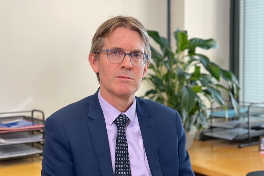 John Chesterman, a white man in wearing glasses and a suit, looks serious.