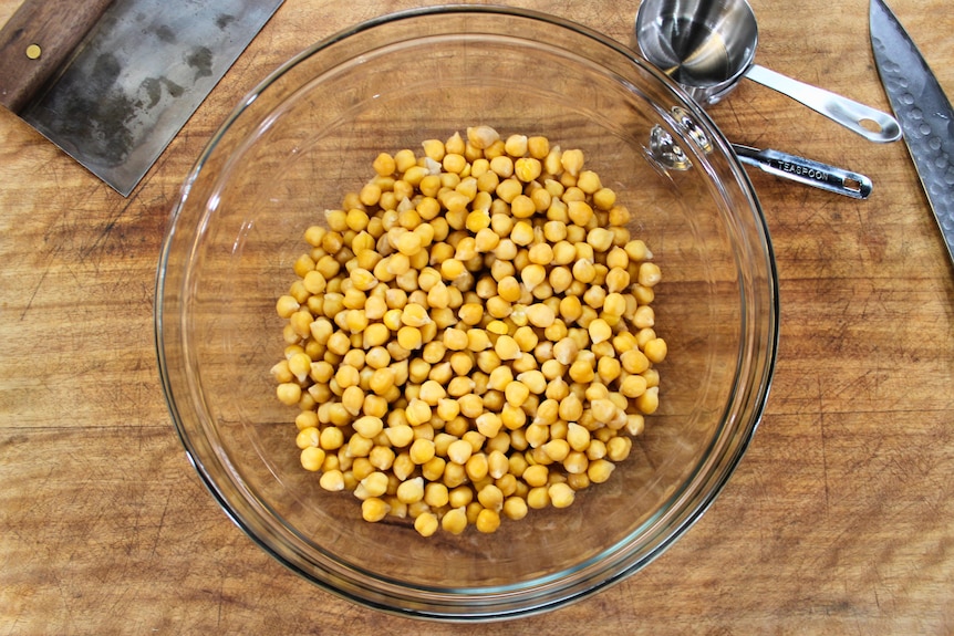 Soaked chickpeas in a glass bowl on a wooden bench.