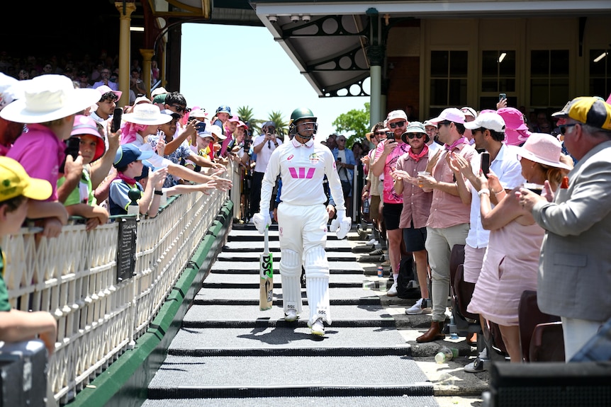 Australia batter walks down the steps at the Sydney Cricket Ground on the way to the field. Fans applaud either side of him.