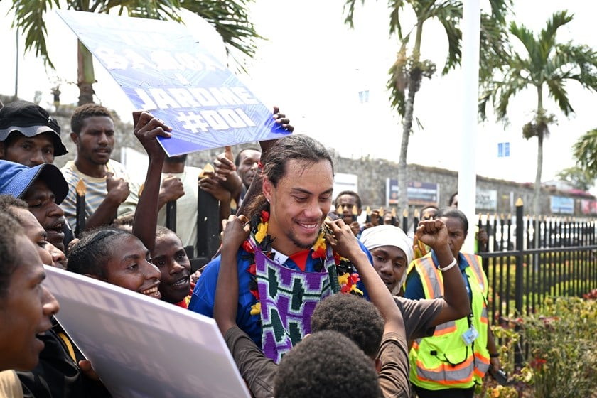 A fan presents Jarome Luai with a bilum  as a welcome gift while others hold banners.