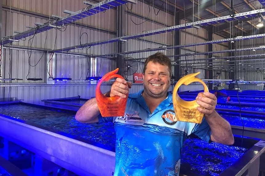 A man in front of a fish tank holding up some awards