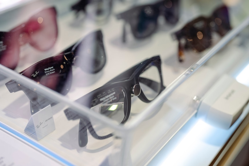Several pairs of smart glasses are lined up in a clear drawer, with the logo of Ray Ban visible on one pair.