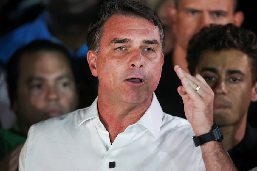Flavio Bolsonaro in a white shirt and wearing a black wristwatch speaking while gesturing with one hand.