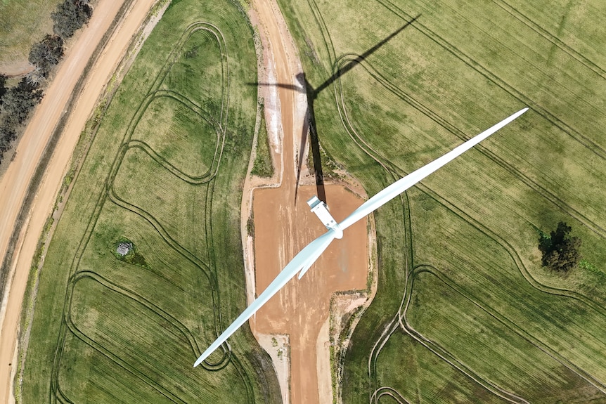 An aerial shot looking straight down at a giant wind turbine and its shadow in a paddock