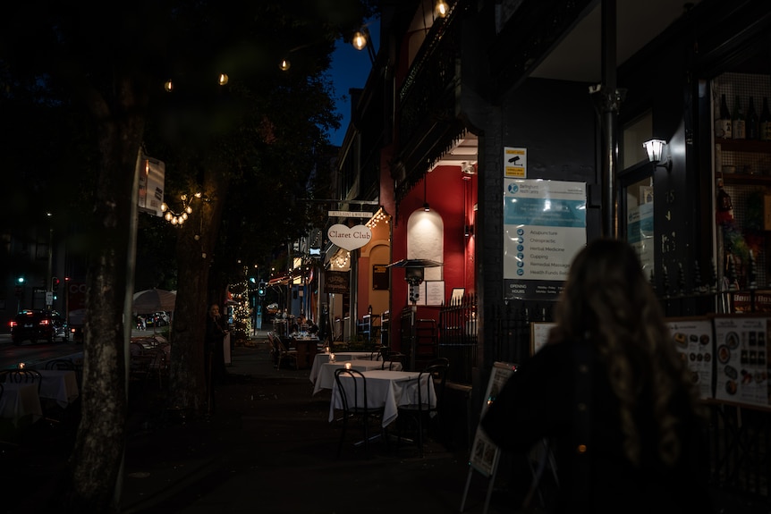 a dark street with restaurant tables and the glow of lights