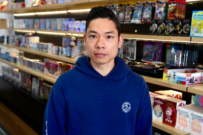 a man in a hoodie stands in front of shelves full of video games and merchandise