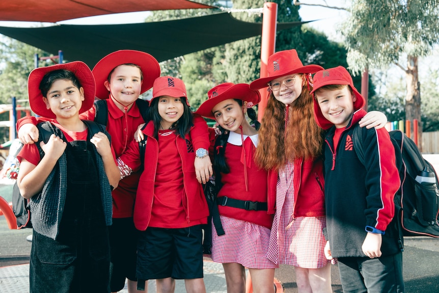 Six students smile as they pose outside in blue and red uniforms, all wearing hats.
