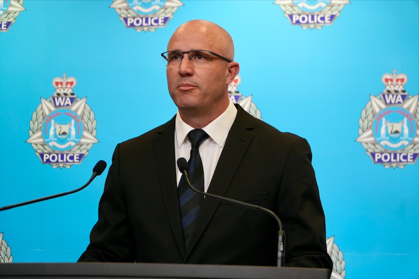 Heath Atkinson stands at a lectern with the WA police logo in the background.