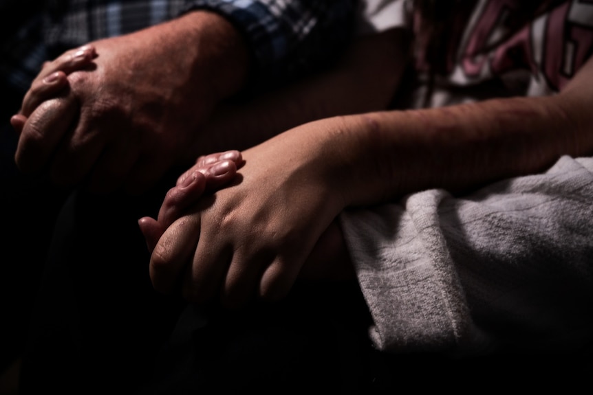 A man and his daughter hold hands on a couch.