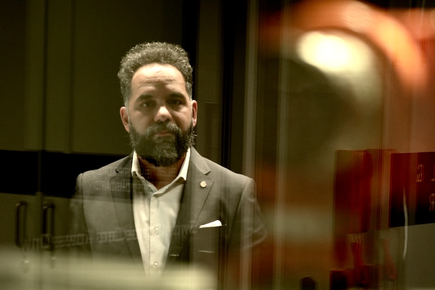 A bearded man wearing a suit is seen standing behind a window.