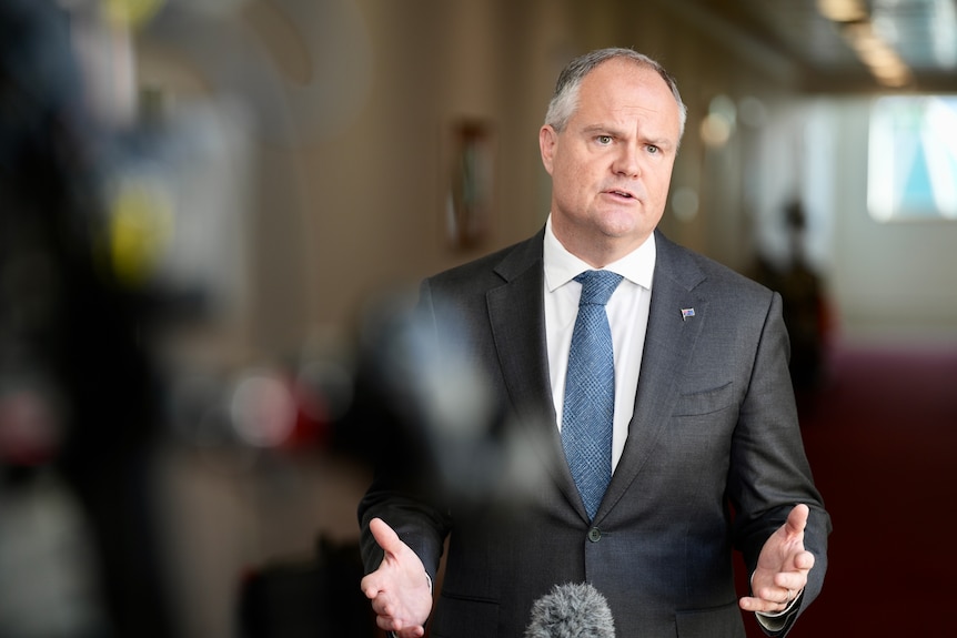 Ted O’Brien at a press conference talking and gesturing with his hands.