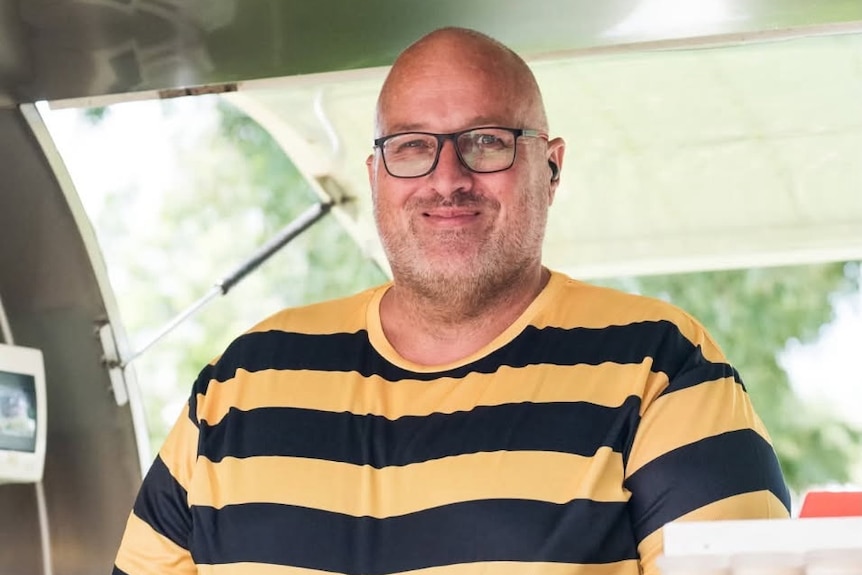 A man dressed similar to a bee smiles while holding a honey jar.