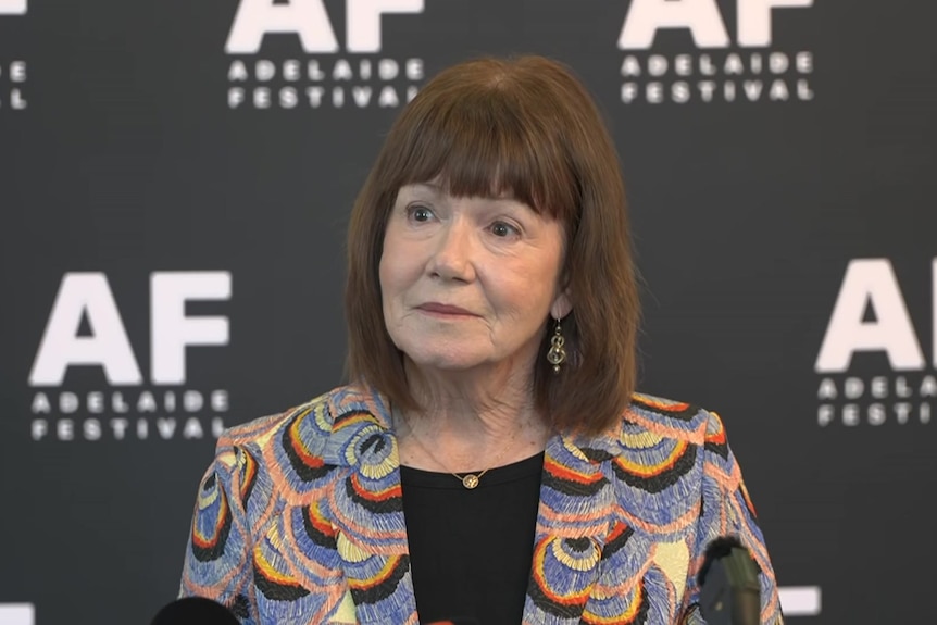A woman in a business suit stands in front of Adelaide Festival banner