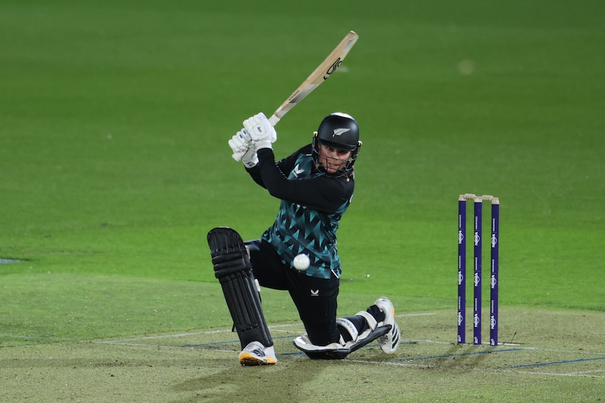 A female New Zealand cricketer is on one knee after hitting the ball