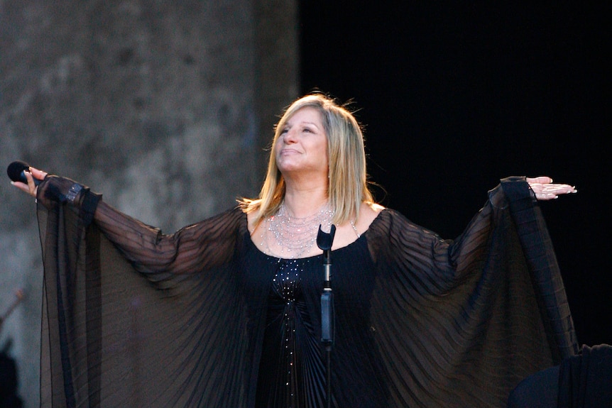 A woman in black holds her hands in a shrug 