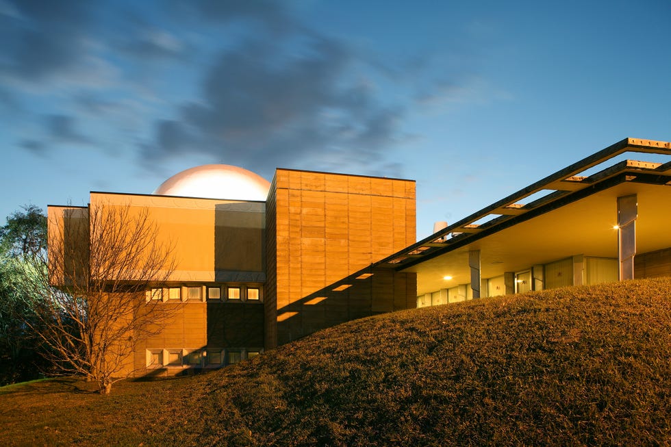 Modern architectural building with a domed structure, illuminated during twilight against a cloudy sky.