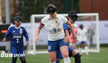 England blind footballer Samantha Gough dribbles with the ball. She wear England kit and her blonde hair is in a plait. She wears blindfold goggles.