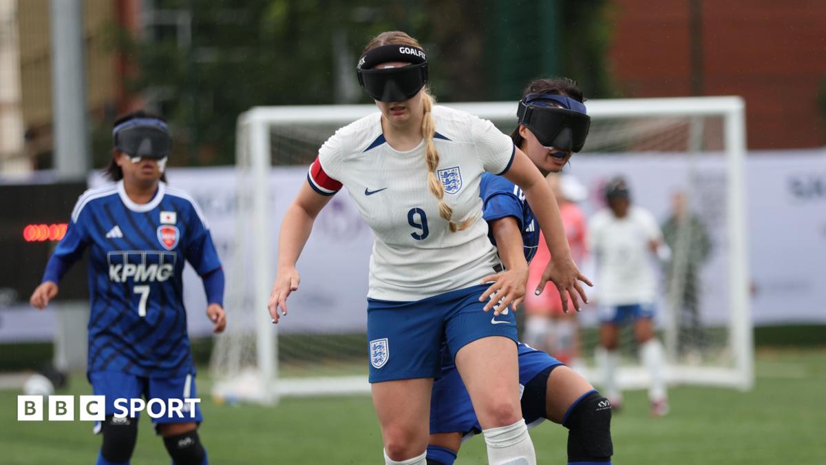 England blind footballer Samantha Gough dribbles with the ball. She wear England kit and her blonde hair is in a plait. She wears blindfold goggles.