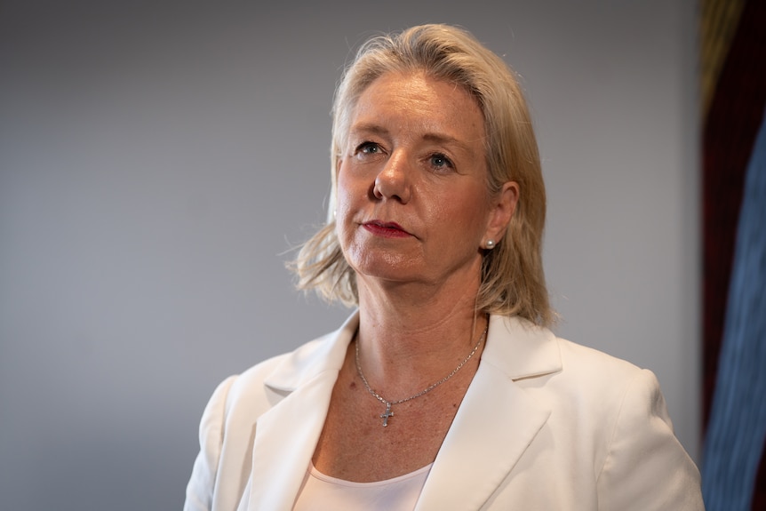 A blonde woman in a white blazer jacket.