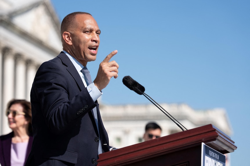 An African American man wearing a suit speaks behind a lectern outside the White House.