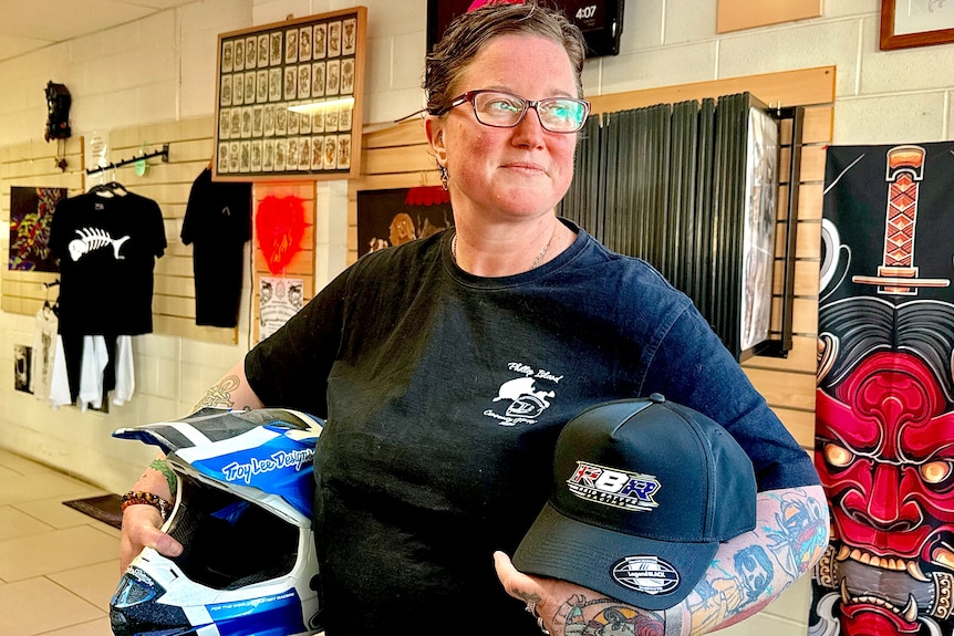 Image of a woman with short hair and glasses, in a black t-shirt, holding a motorbike helment.