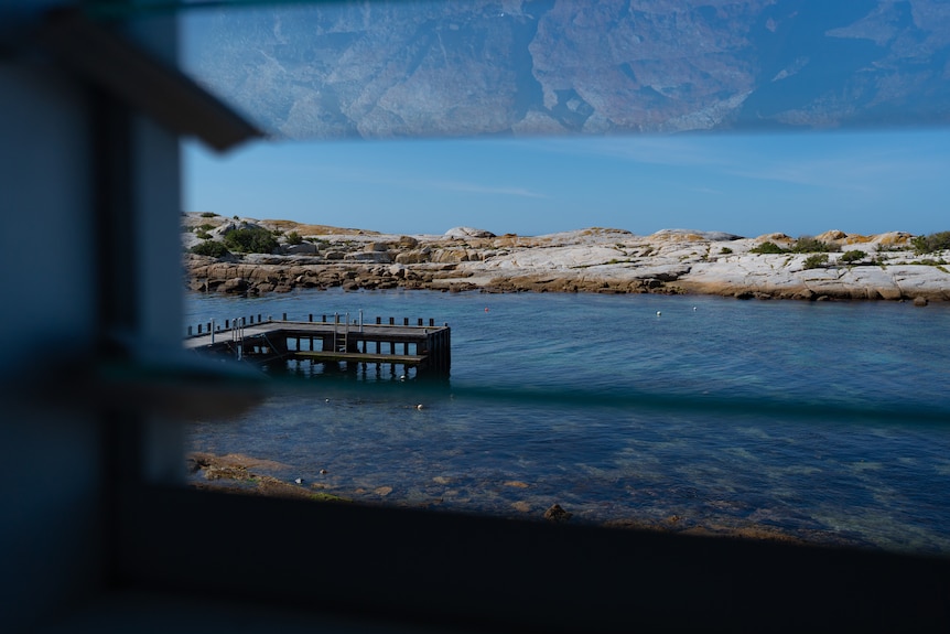 An old oyster hatchery sitting directly on the ocean on a clear day, there are rocks with orange lichen and a distillery