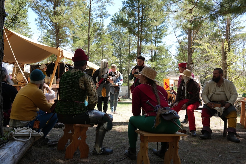 A group of living history military simulation reenactors eat a meal sitting in a circle 