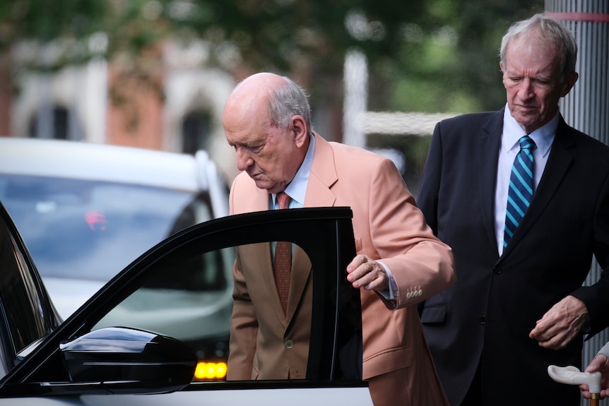 Mr Jones in a peach-coloured blazer and tie getting out of a car and about to close the car door.