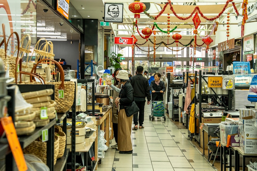 People dressed in jumpers and pants shop in food stores at a suburban shopping centre.