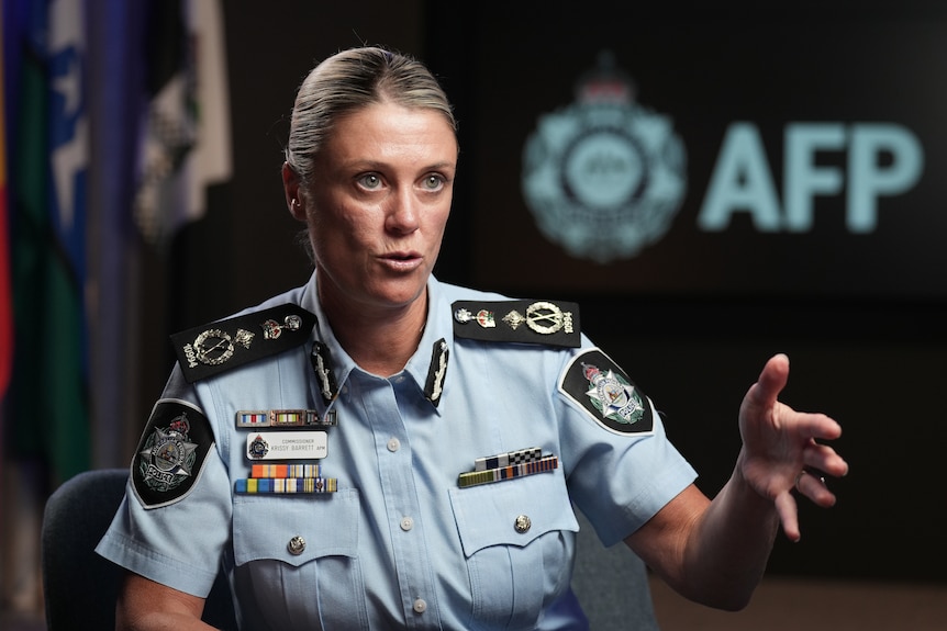 A blonde woman in police uniform gesticulating with her left hand with flags and AFP sign in background.