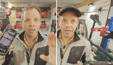 A man holds a smartphone and gestures in a workshop with tools and a bicycle in the background.