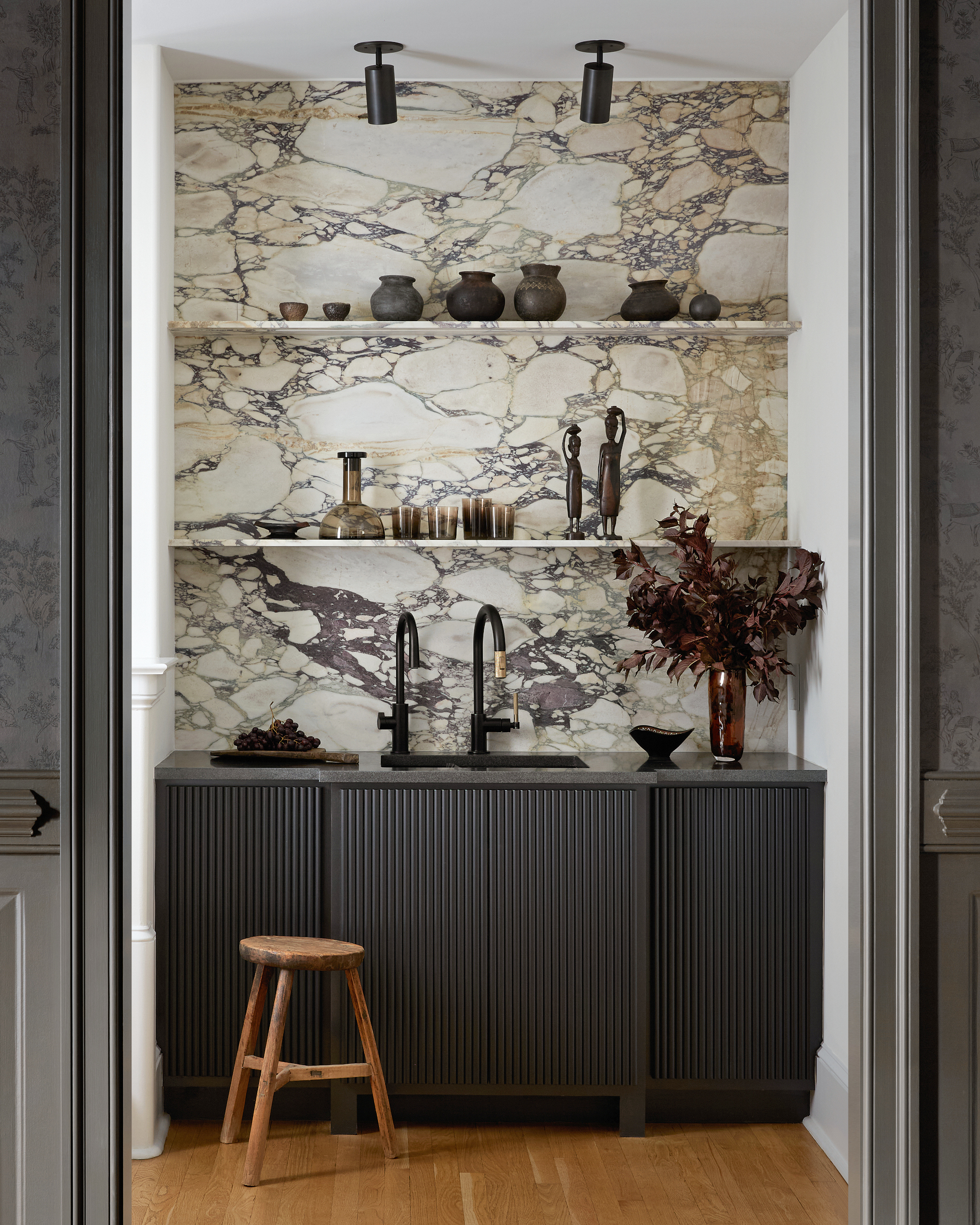 Wet bar with black fluted unit, marble backsplash and shelving, black taps and wood stool