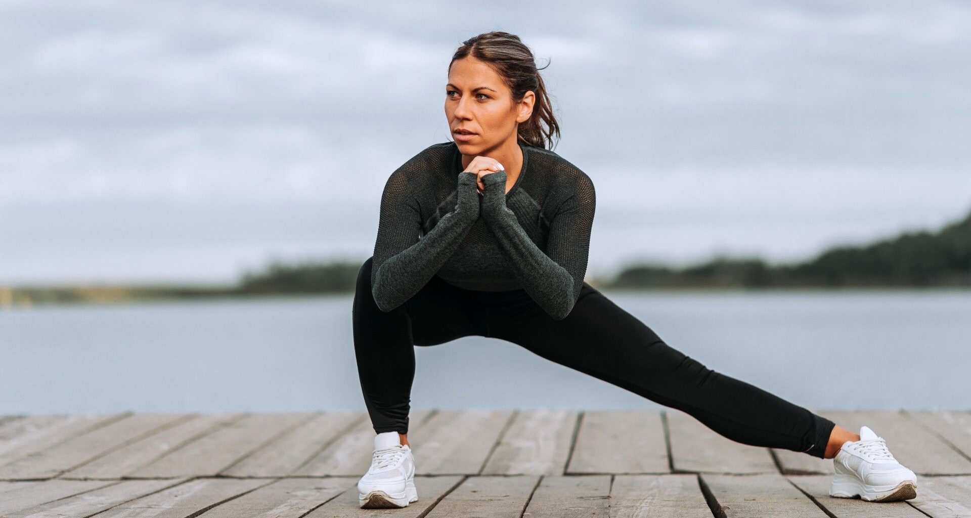 Woman performing a Cossack squat with right knee bent and left knee extended with backdrop of a river