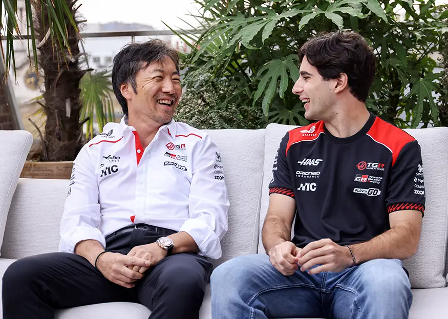 Haas team principal Ayao Komatsu and newly signed 2027 Formula 1 driver Rafael Camara sitting together and laughing during a team photo session.