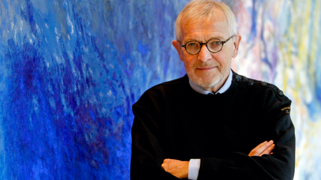 older man in glasses against a blue background