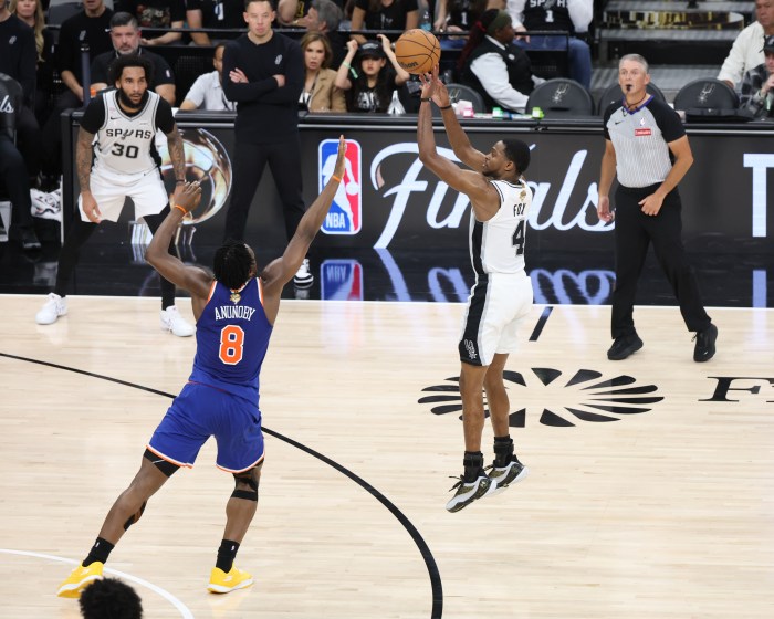 De'Aaron Fox attempts a 3-point basket while a defender puts his arm up to contest.