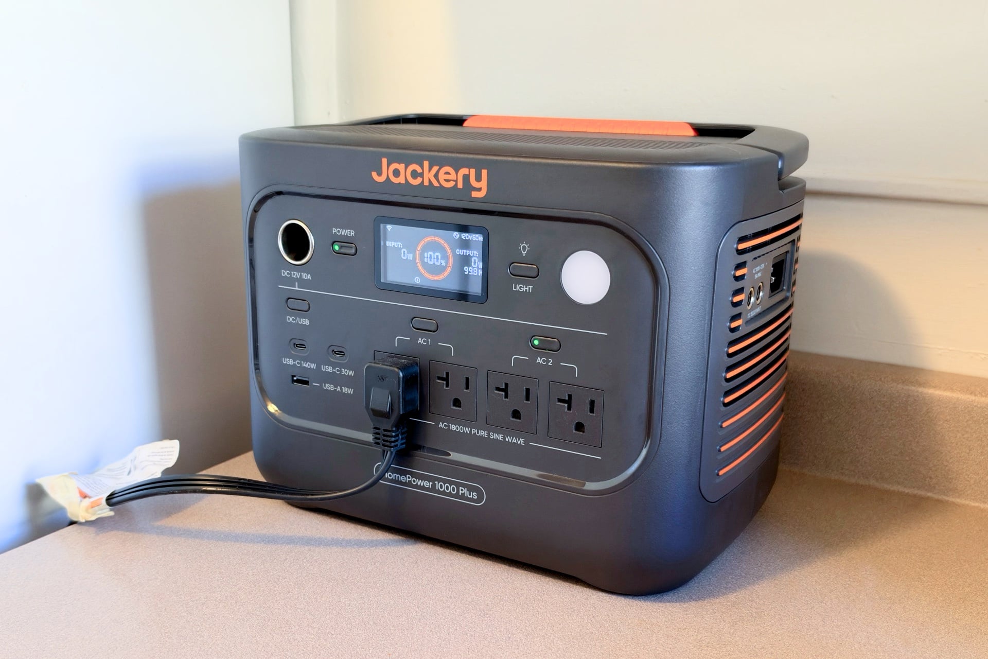Picture of the HomePower 1000 Plus v2 next to a refrigerator, with the appliance plugged into it.