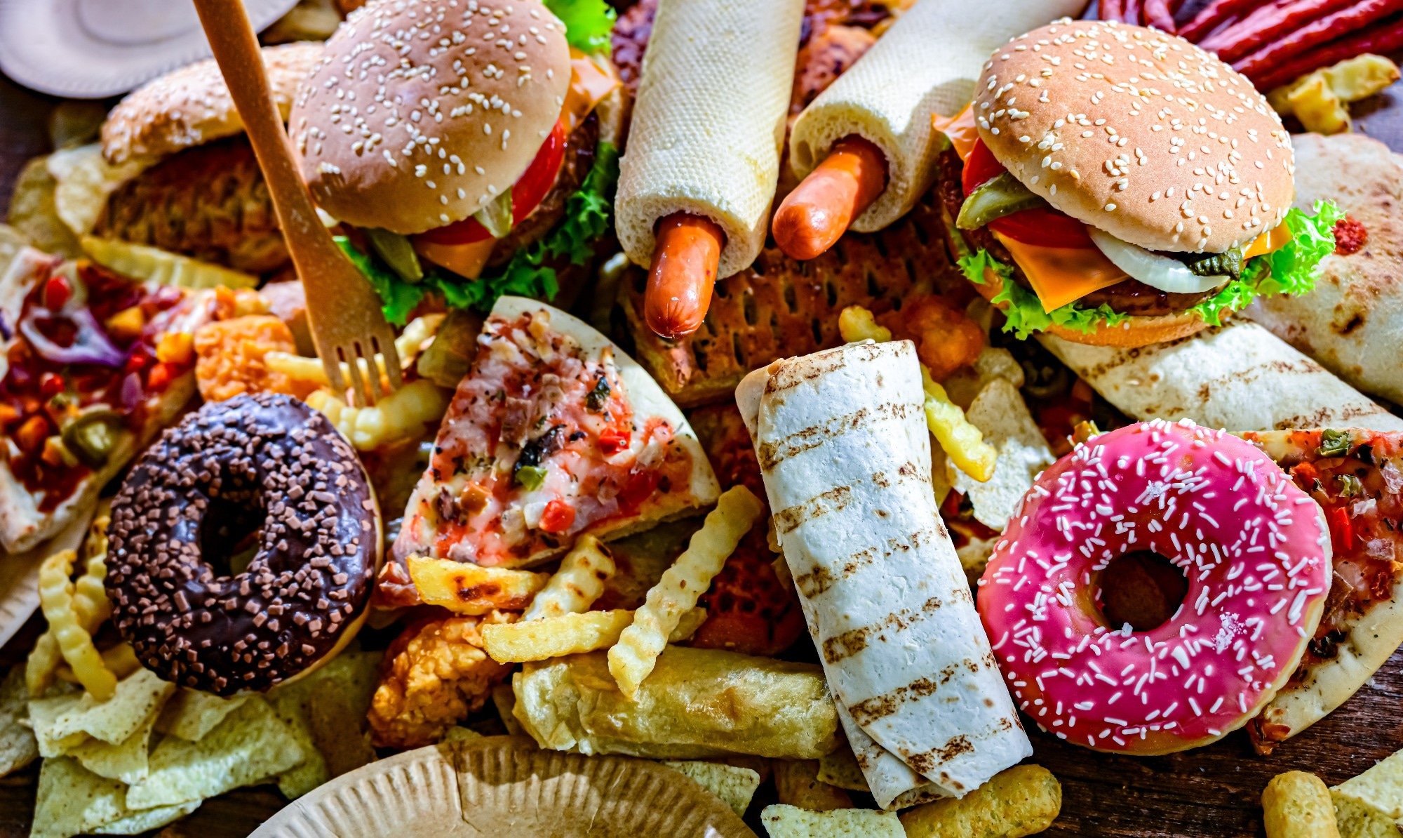 Assortment of ultraprocessed foods, including burgers, hot dogs, pizza, fries, and colorful doughnuts.