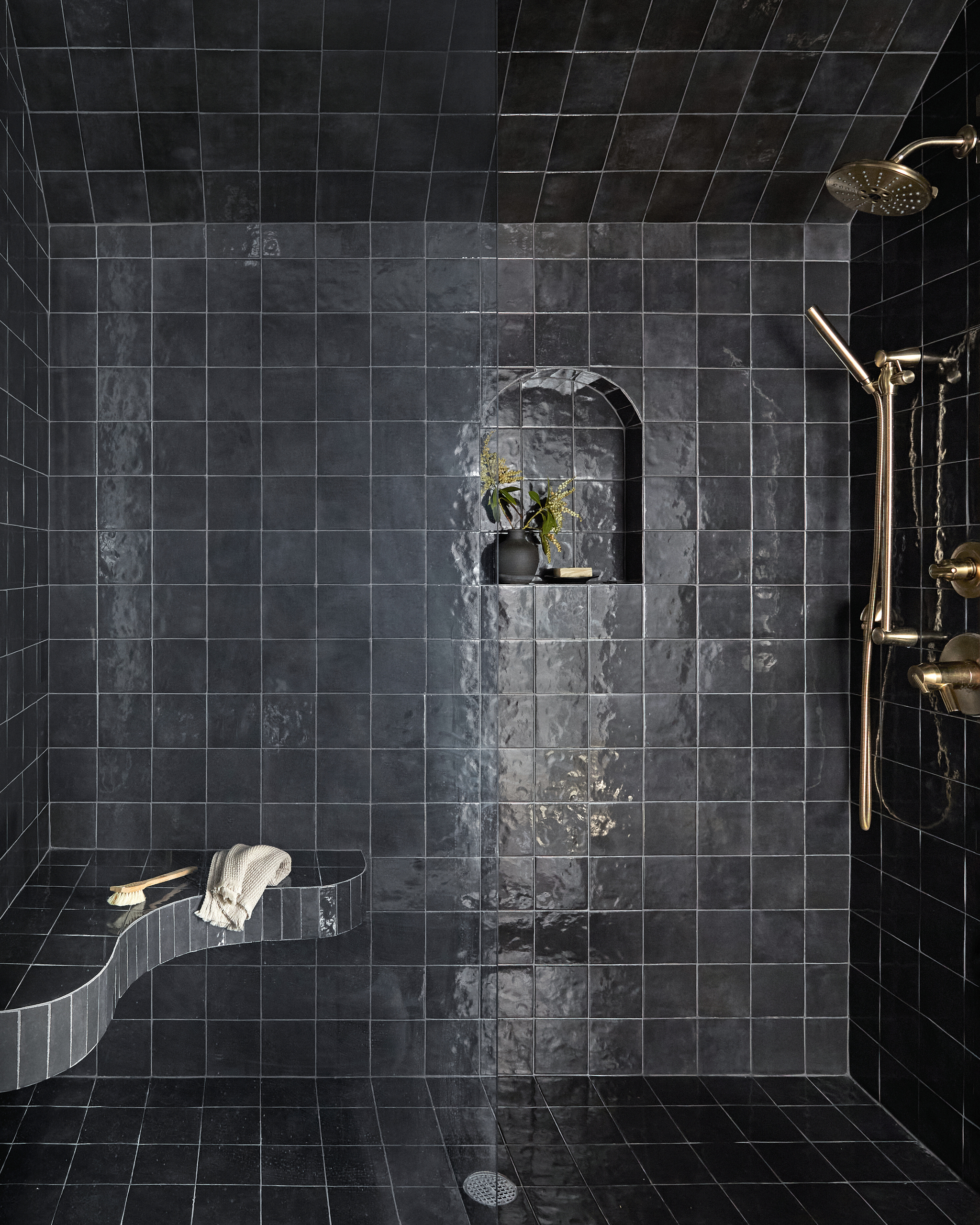 Shower area with black zellige tiles and curved shower bench