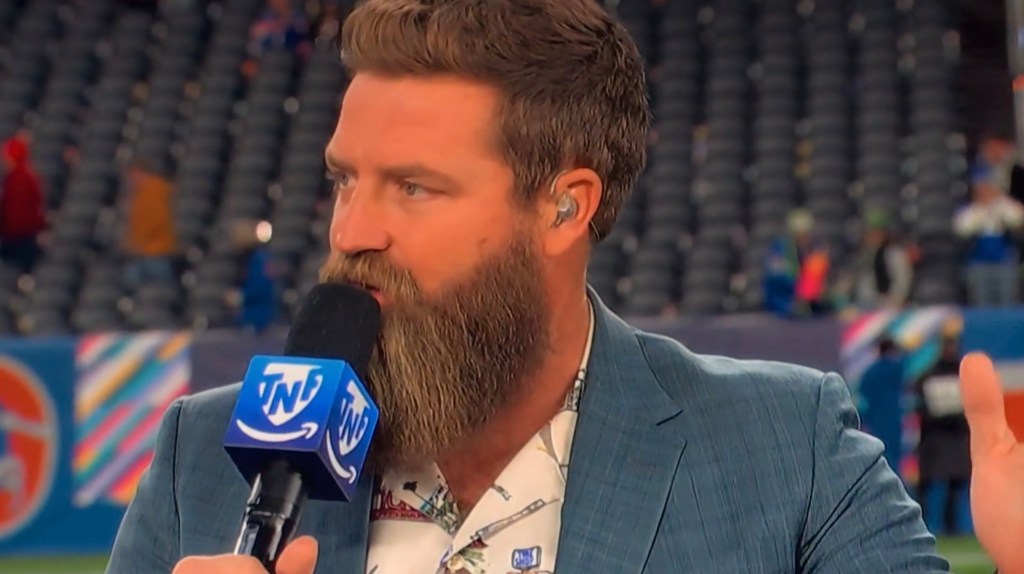 Ryan Fitzpatrick speaking into a microphone with a TNF logo on a football field.