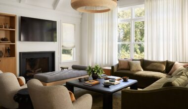 White living room with olive green velvet corner sofa, two beige armchairs, black square coffee table, grey ottoman and black fireplace