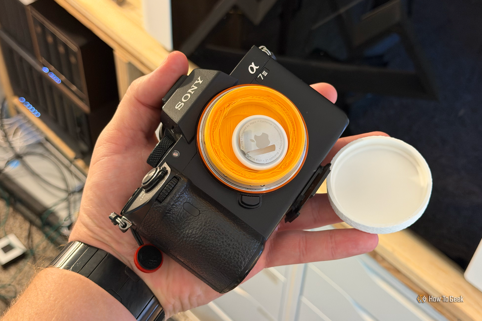 A person holding a Sony A7III camera with a 3D printed lens cap that is holding an AirTag.